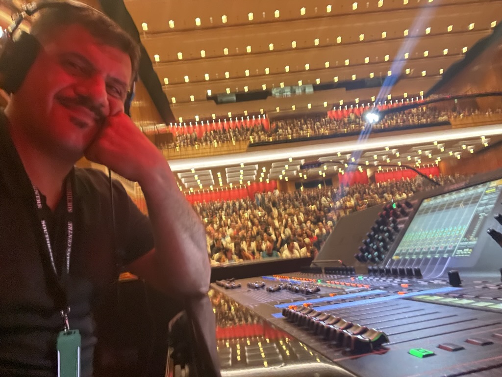 Luigi at the desk with the concert hall audience behind him
